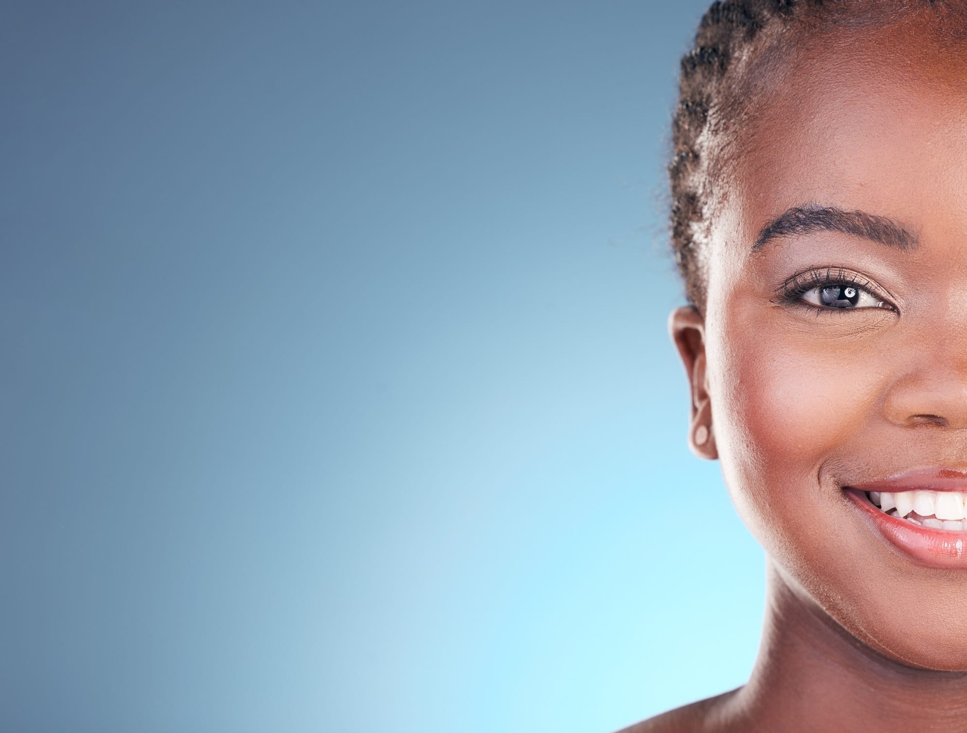 Partial view of a dark-skinned woman’s face. She smiles at the camera, proud of her beautiful, rejuvenated complexion.