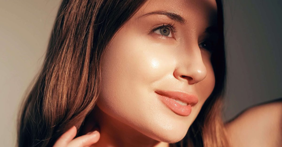 A Beautiful Woman, Partially Lit By Sunlight, Shows Off Her Rejuvenated Skin Thanks To The Power Of Anti-aging Facials.