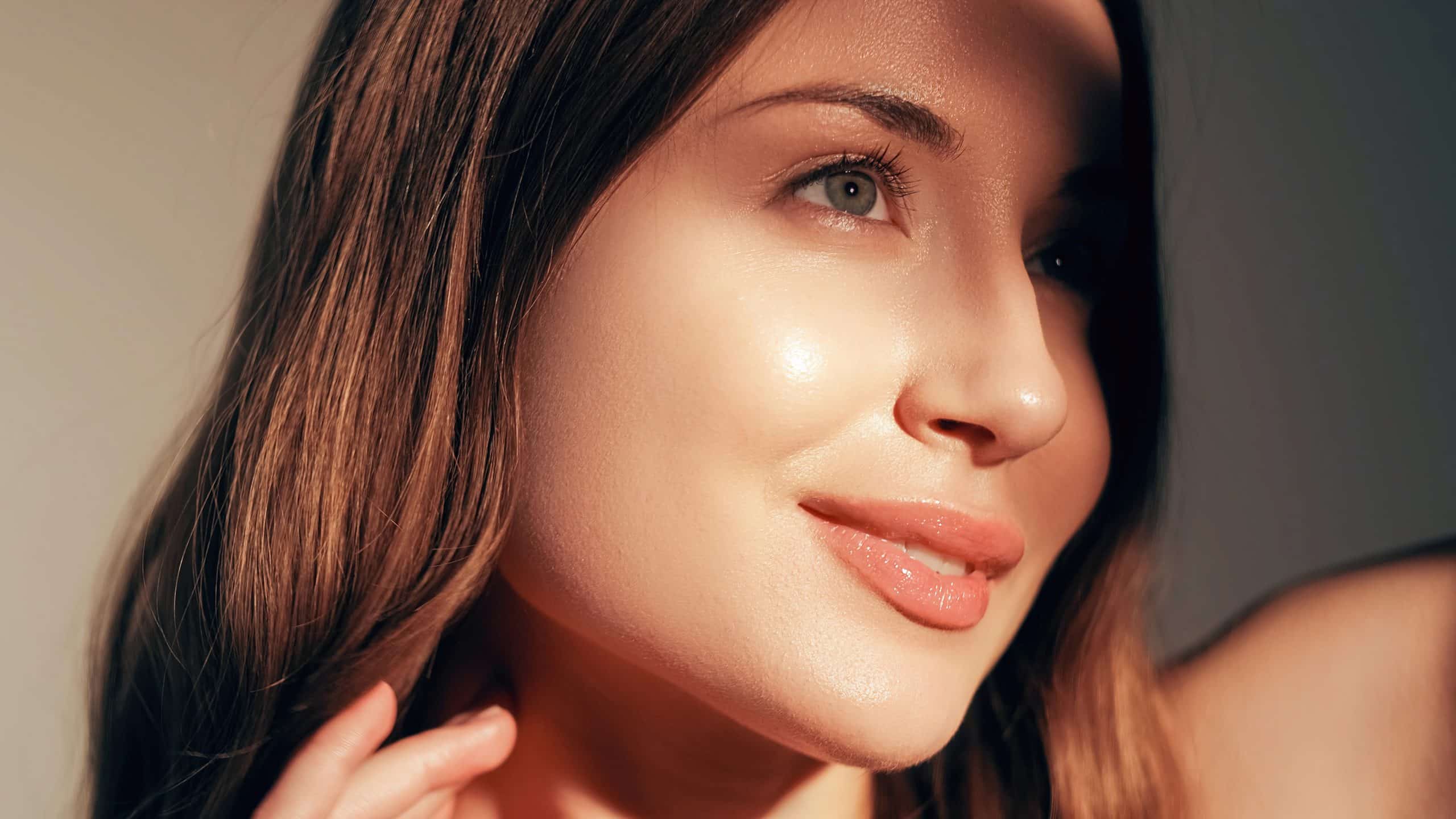 A beautiful woman, partially lit by sunlight, shows off her rejuvenated skin thanks to the power of anti-aging facials.