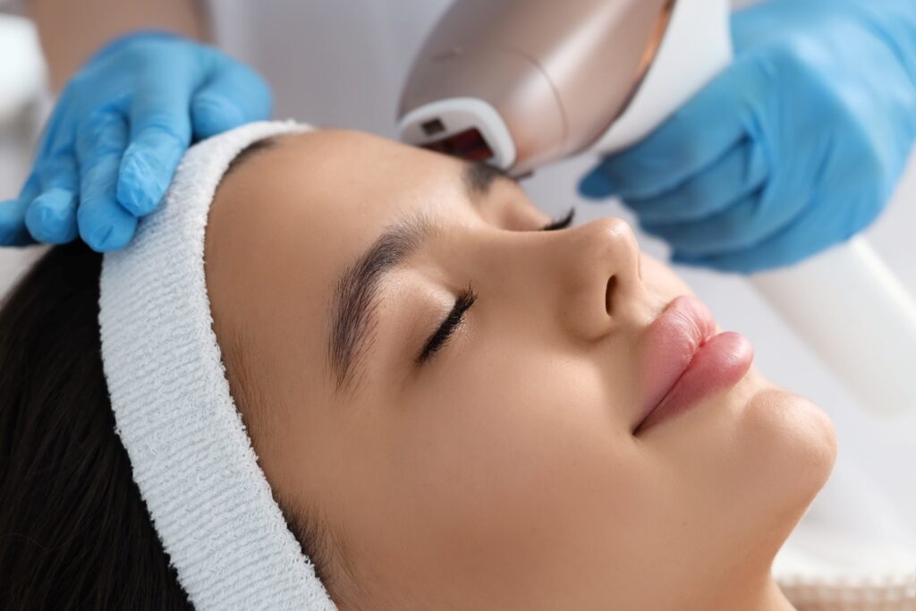 A woman reclining with her eyes closed while she gets BBL and Moxi laser treatment.