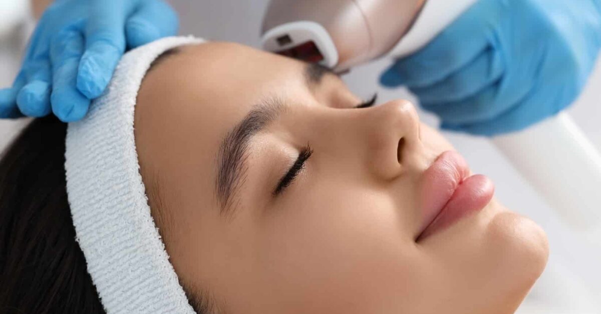 A woman reclining with her eyes closed while she gets BBL and Moxi laser treatment.